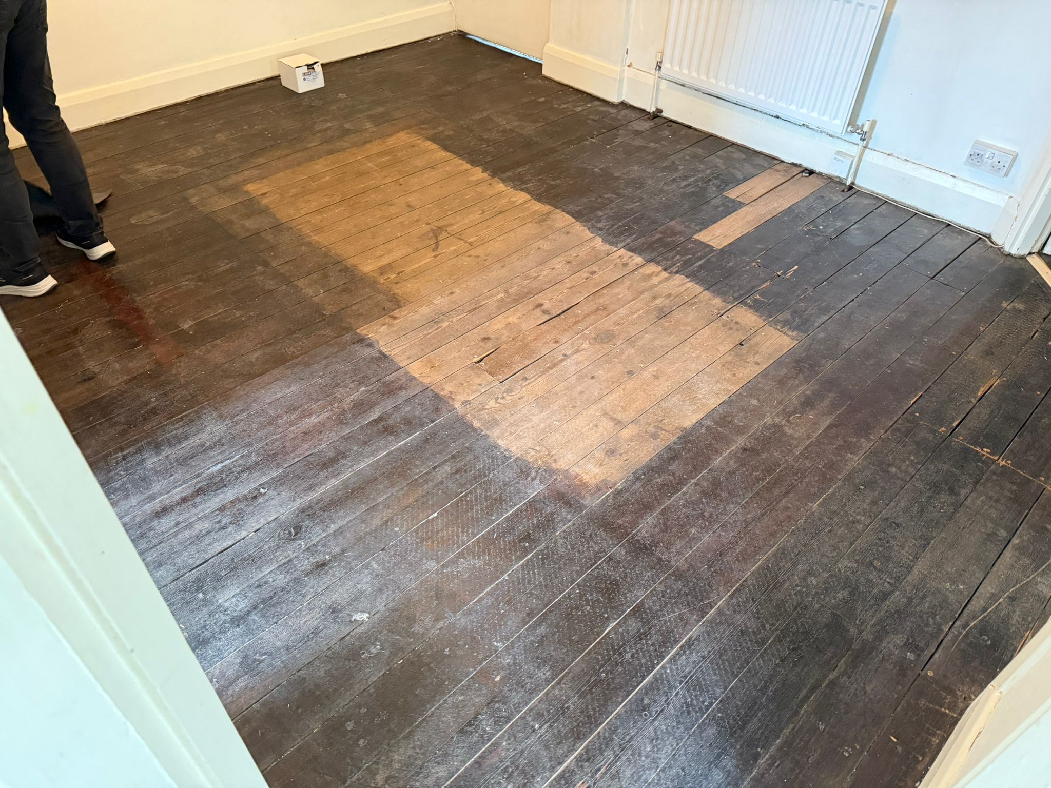 Wood Floor Sanding mid-sanding on Victorian pine floorboards (softwood tongue-and-groove), with a rectangular test pass exposing clean timber among dark, worn boards.