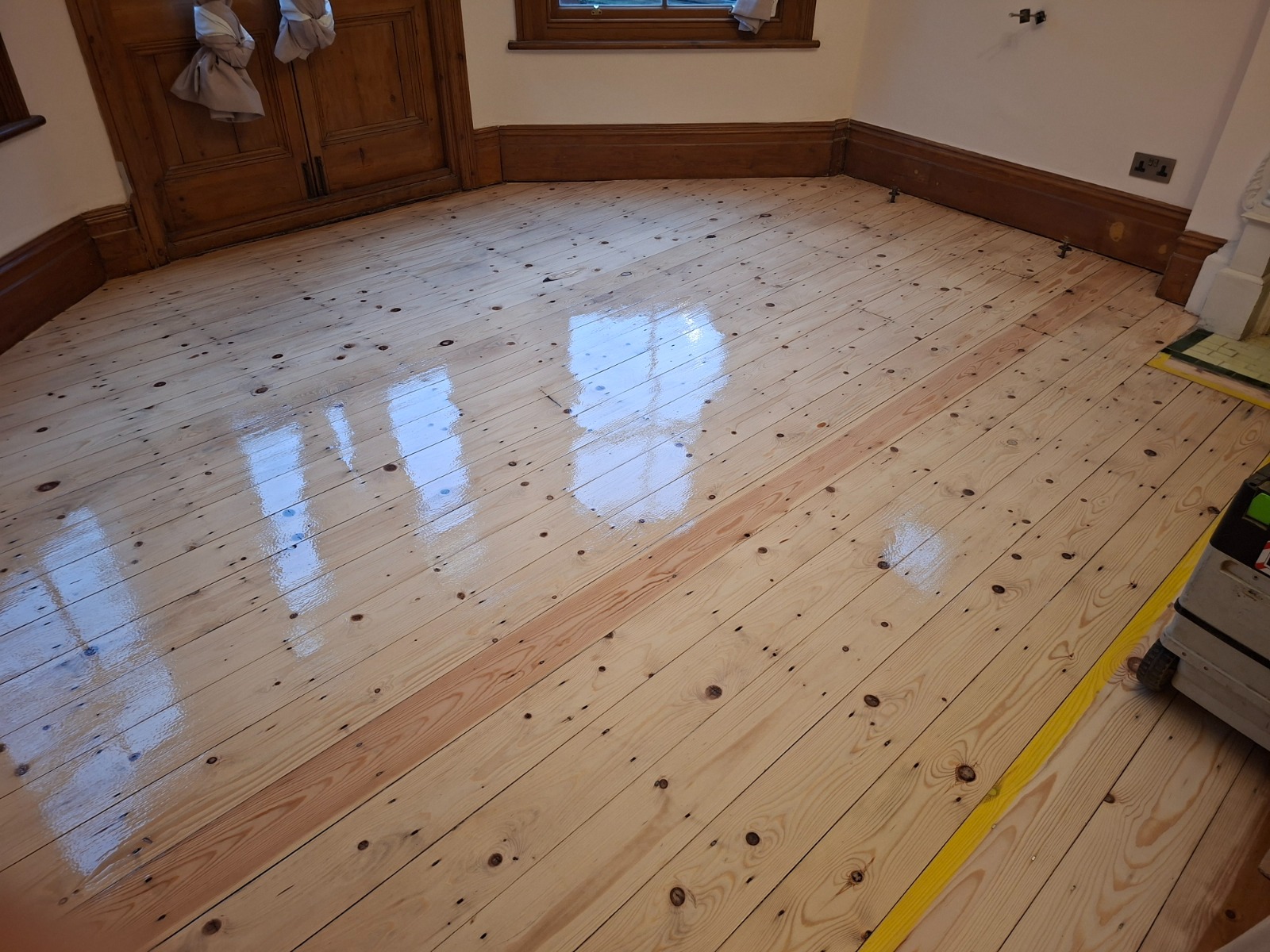 Wood Floor Sanding results on pale pine softwood floorboards in a bay window room, freshly lacquered with a high-gloss finish.