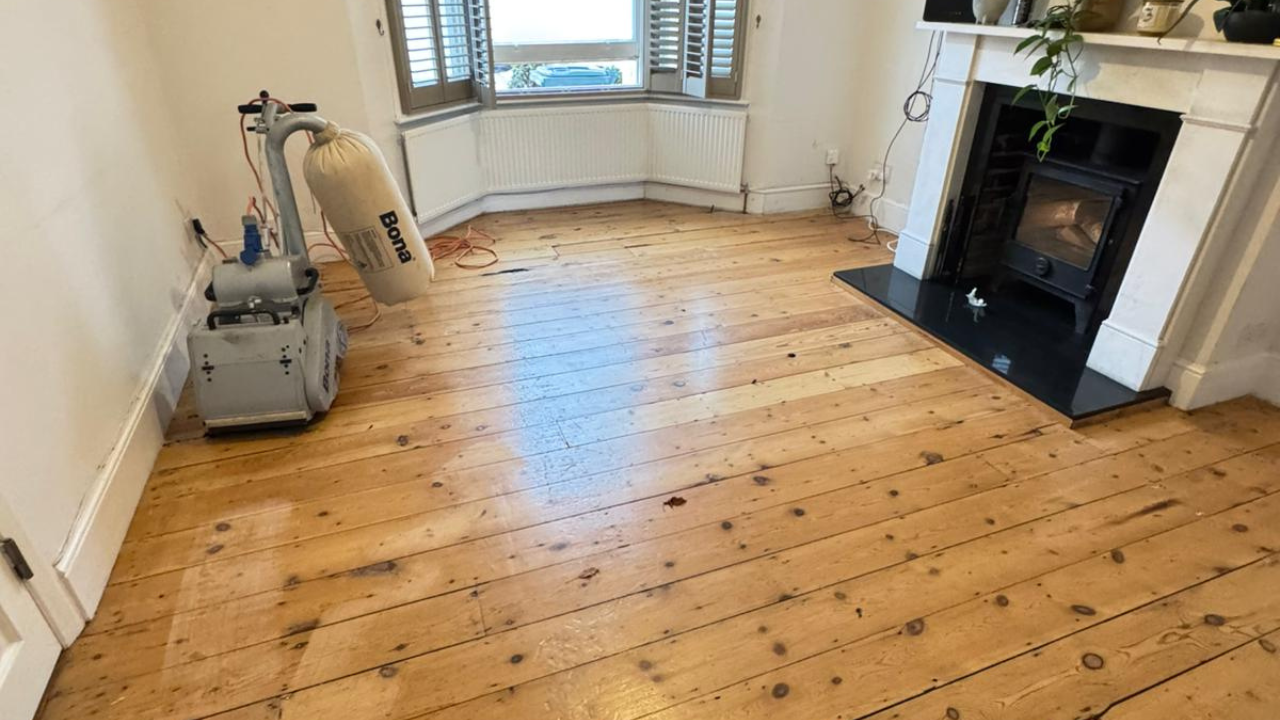 Wood Floor Sanding in a living room on original pine softwood floorboards with a Bona belt sander by the wall.