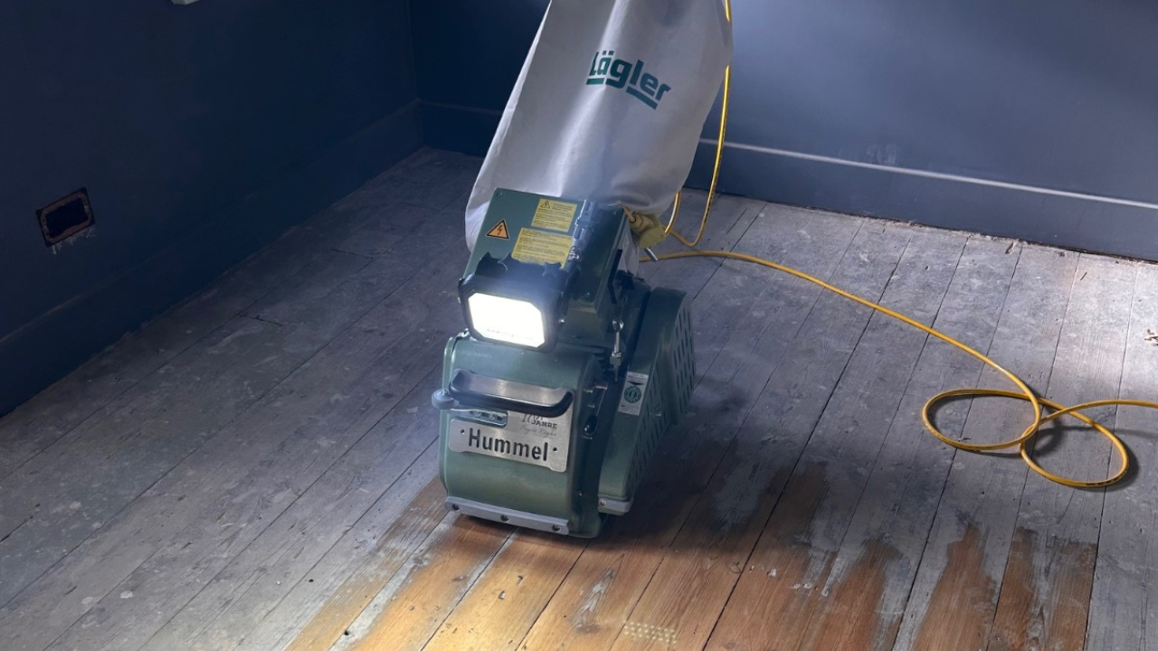 Wood floor sanding in progress with a Hummel belt sander restoring old softwood pine floorboards.