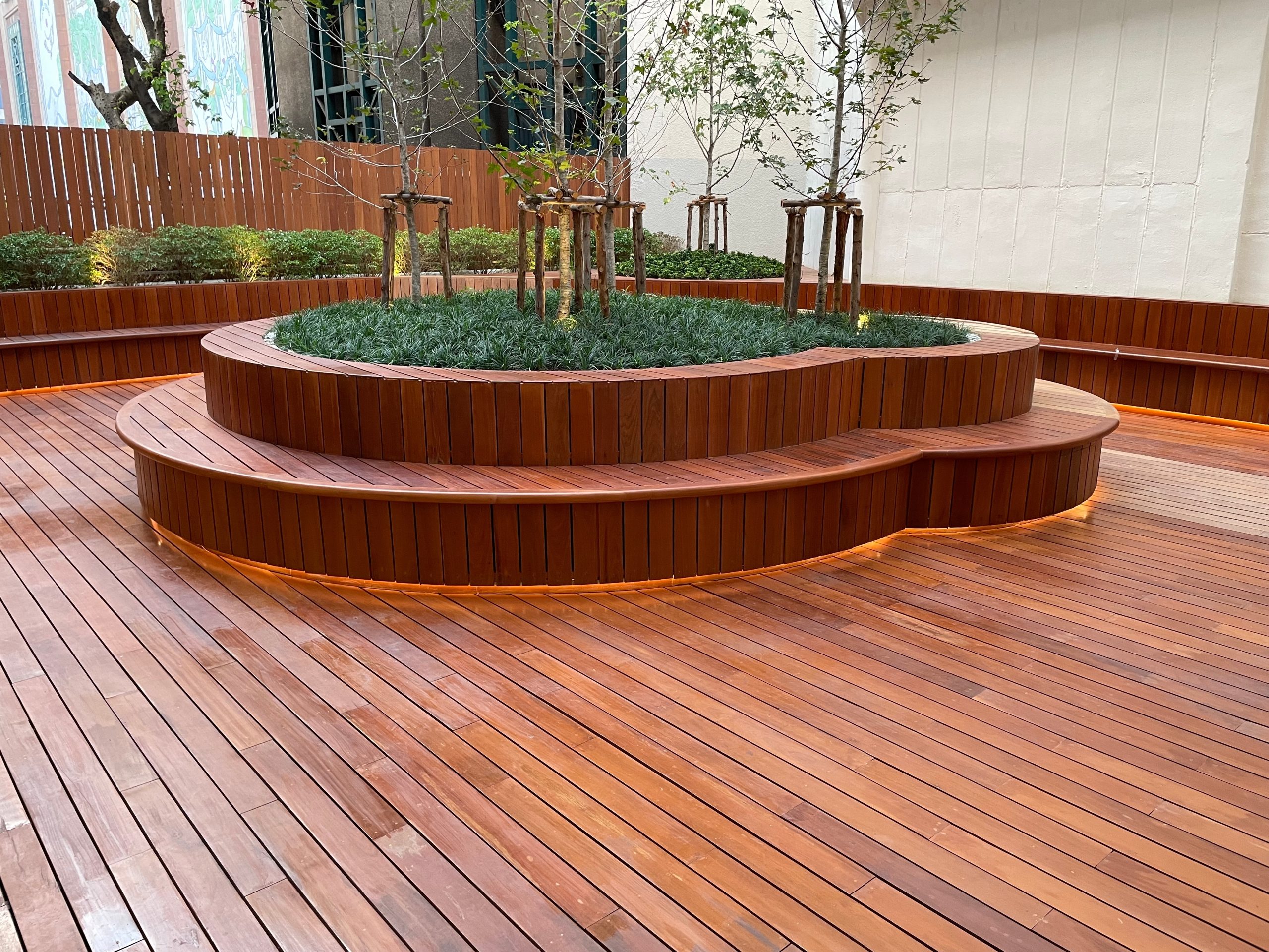 Deck Sanding in City – beautifully restored hardwood courtyard deck floor with curved timber seating and raised planter after professional sanding and finishing.