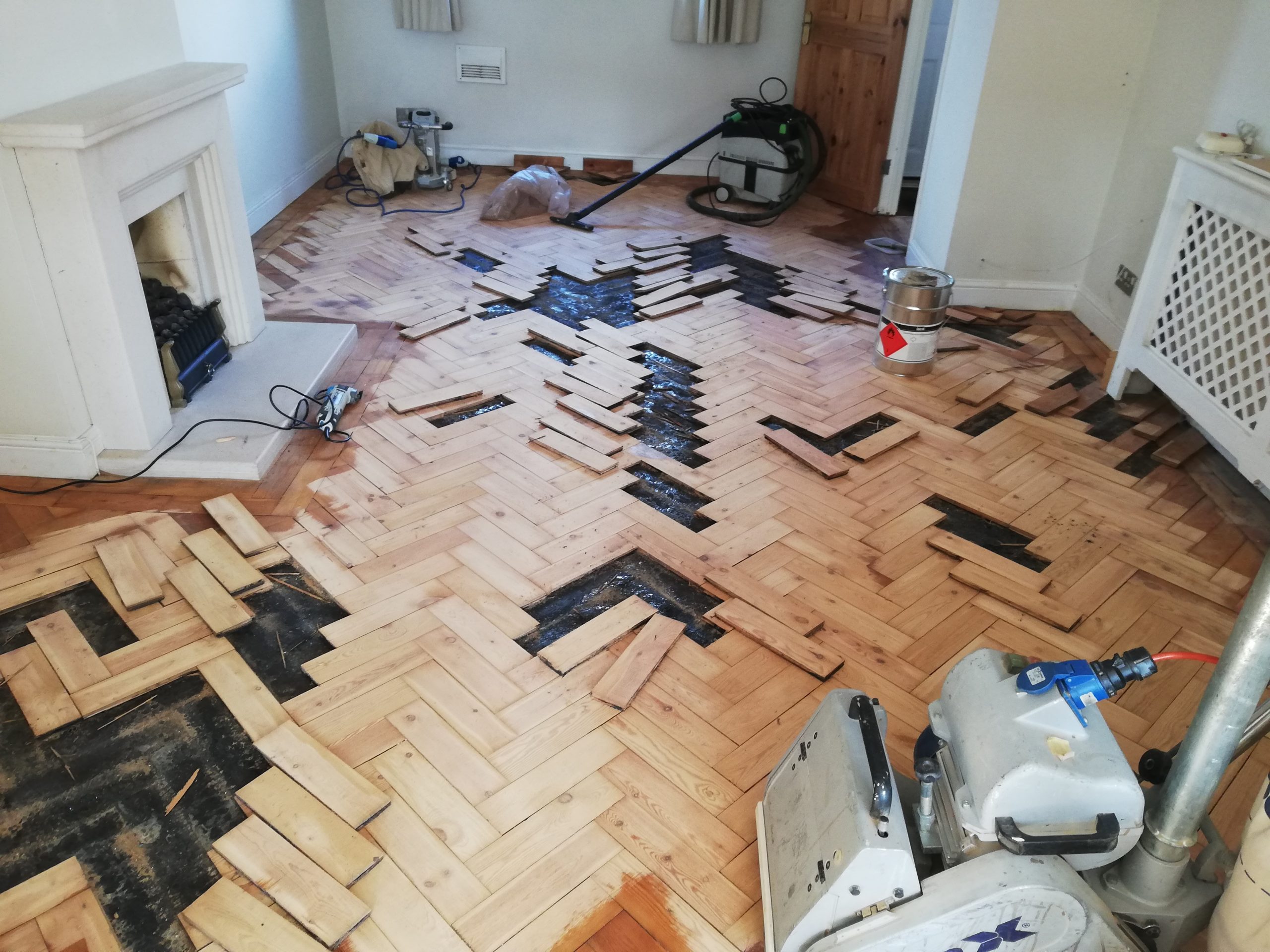 Parquet Floor Restoration in progress on a solid oak herringbone parquet floor with damaged wooden blocks being lifted, repaired and prepared for refinishing.