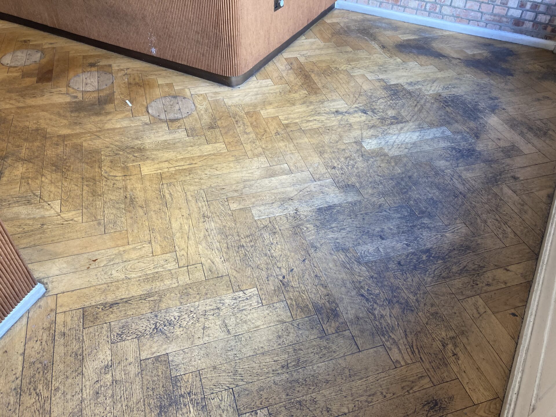 Parquet Floor Restoration for an oak herringbone parquet wood floor showing worn finish, surface staining and repair work needed before sanding and refinishing.