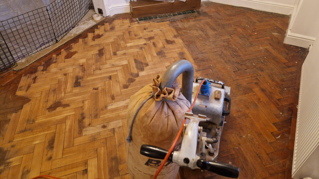 Parquet Floor Restoration in progress on an oak herringbone parquet wood floor with professional sanding machine removing worn finish and surface marks